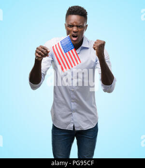 Young african american man holding USA flag contrarié et frustré de crier avec colère, fou et hurlant de main levée, la colère concept Banque D'Images