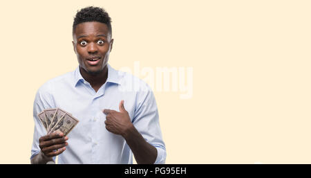 Young african american businessman holding dollars avec surprise face à face à lui-même Banque D'Images