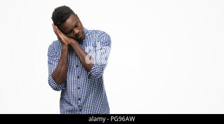 Young african american man wearing blue shirt fatigué dormir rêver et posant avec les mains tout en souriant avec les yeux fermés. Banque D'Images