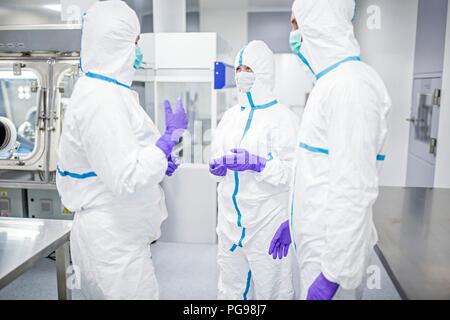 Des techniciens de laboratoires équipés de vêtements de protection et de masques dans un laboratoire qui doit maintenir un environnement stérile. Banque D'Images