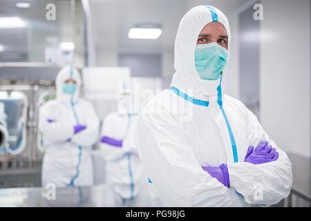 Des techniciens de laboratoires équipés de vêtements de protection et de masques dans un laboratoire qui doit maintenir un environnement stérile. Banque D'Images