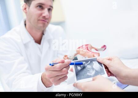 Consultation des cliniques de fertilité. Médecin à l'aide d'un modèle de l'appareil reproducteur féminin d'expliquer une échographie du patient. Banque D'Images