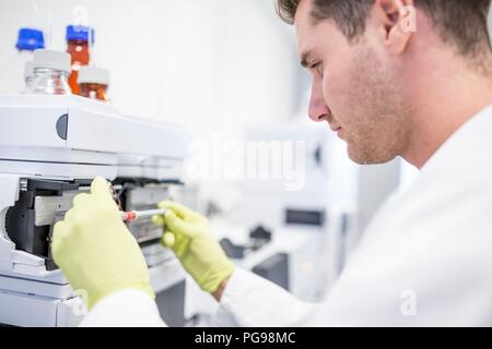 Mise technicien une colonne en verre contenant une solution d'étalonnage à un spectromètre de masse. La spectrométrie de masse passe par des champs magnétiques et électriques pour séparer les composants d'un échantillon en masse et de charge. Cela permet aux chercheurs de déterminer la composition élémentaire de l'échantillon. Banque D'Images