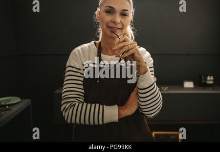 Portrait of young woman standing bijoutier dans son atelier en regardant la caméra. Woman wearing apron en orfèvrerie fabrication de bijoux studio. Banque D'Images