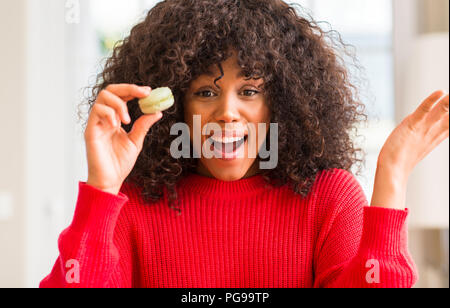 African American Woman holding macaron très heureux et excité, lauréat expression célébrant la victoire de crier avec grand sourire et mains levées Banque D'Images