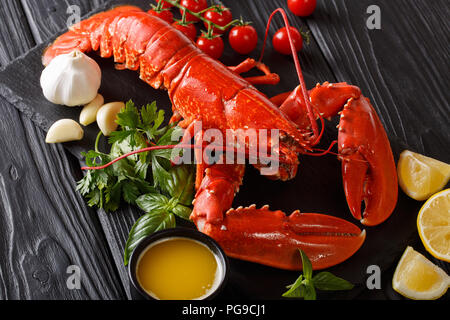 Gros plan du homard fraîchement préparé avec du citron, l'ail, tomates fraîches et d'herbes sur une table horizontale noire. Banque D'Images