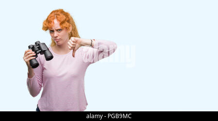 Jeune femme rousse binoculars with angry face, signe négatif montrant non avec vers le bas, le rejet de la notion Banque D'Images