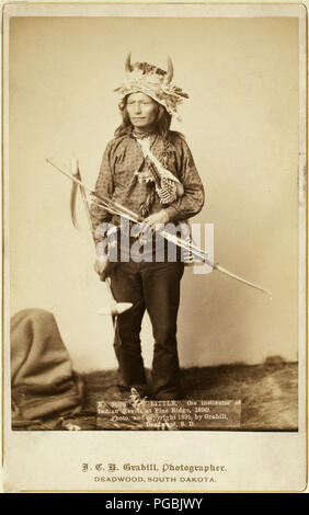 Peu d'Oglala, leader du groupe, portrait studio, debout, face à l'avant, portant une coiffe de l'avertisseur sonore, pantalon et chemise, et la tenue d'arc, de flèches et de tomahawk. Banque D'Images