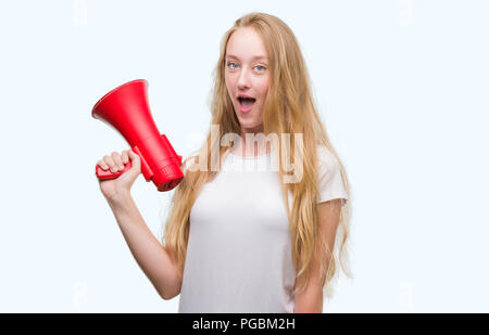 Adolescent Blond woman holding megaphone peur sous le choc face à une surprise, de peur et d'excité avec crainte expression Banque D'Images