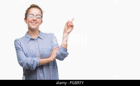 Jeune femme d'affaires blonde avec un grand sourire sur le visage, en pointant avec la main et le doigt sur le côté regardant la caméra. Banque D'Images