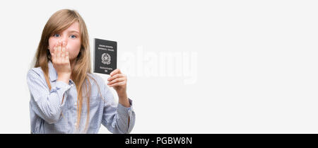 Jeune blonde toddler holding passeport italien couvrir la bouche à part choqué avec honte pour erreur, expression de la peur, peur en silence, secret conc Banque D'Images