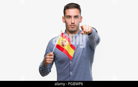 Beau Jeune homme tenant un drapeau de l'Espagne avec le doigt pointant à l'appareil photo et à vous, signe de main, geste positif et confiant de l'avant Banque D'Images