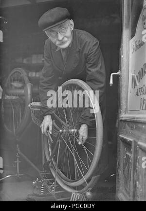 1940 l'homme de réparation de vélos. Un homme âgé à la porte de son atelier de réparation de vélos. Il a vélo à l'envers et travaille sur la dépose de la roue arrière. La Suède Mai 1940. Kristoffersson 132-11 Photo Banque D'Images