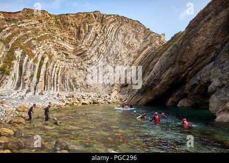 / Lulworth Dorset - 22 août 2018 : dans l'ombre d'un pli géologique sur la côte du Dorset au trou d'escalier personnes palette et participer à coasteering Banque D'Images