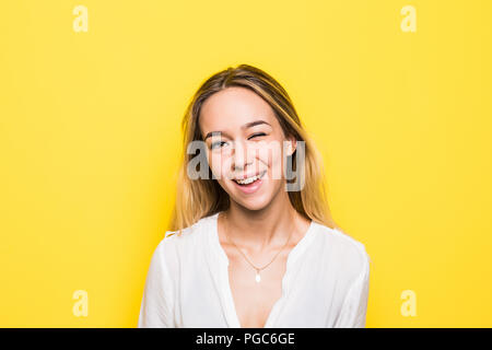 Jeune femme blonde habillée sombre désinvolture making faces at camera, clignotement isolé sur fond jaune Banque D'Images