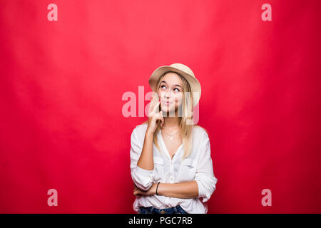 Portrait de jeune femme portant au chapeau de paille et de toucher le menton avec vue de rêve ou de couvaison, isolé sur fond rouge Banque D'Images