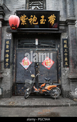 Porte d'une maison traditionnelle à Pingyao, Chine, avec motos et les écrits chinois Banque D'Images