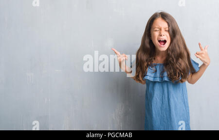 Les jeunes enfants hispaniques plus grunge mur gris criant avec crazy expression faisant rock symbole avec les mains. Music star. Concept lourd. Banque D'Images