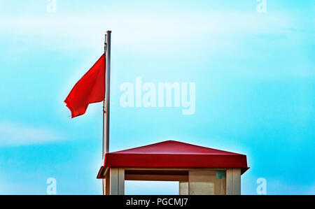 Un drapeau d'avertissement rouge vif près d'une tour de sauvetage , bleu et ciel nuageux , Banque D'Images