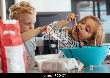 Les petits enfants mixer dans un bol pour la cuisson, avec girl licking une cuillère. Les enfants la cuisson dans la cuisine. Banque D'Images