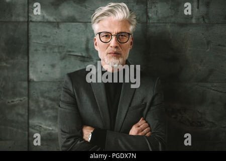 Portrait of businessman standing sur un arrière-plan gris. Beau mâle dans les verres debout avec les bras croisés et regarder ca Banque D'Images