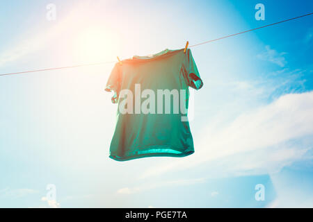 Photo de T-shirt vert accroché sur fond de ciel bleu contre la corde. Banque D'Images