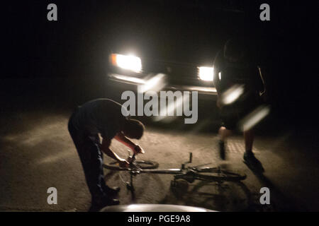 Dangers de la ville de nuit : Les gens déposer un vélo à la route après l'accident de voiture, lumineuse, environnement sombre Banque D'Images