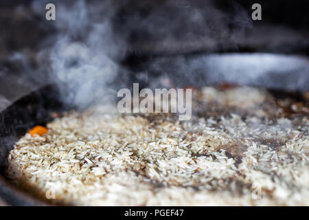 Pour la cuisson du riz pilaw ou paella dans chaudron en fer sur feu ouvert. La fumée et la vapeur. La préparation des aliments savoureux processus extérieur arrière-plan. Banque D'Images