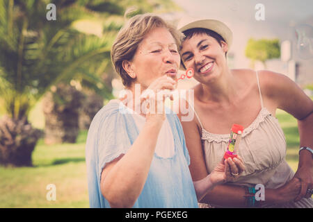 Deux âges différents comme mère et fille jouer ensemble dans l'activité de loisirs de plein air avec des bulles de savon. profiter de la journée dans le parc avec plante verte Banque D'Images