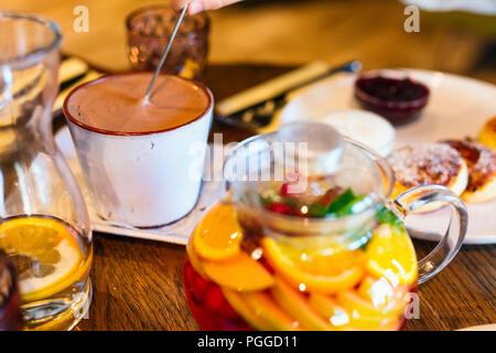 Plateau avec des baies sauvages et des fruits en théière en verre et tasse de chocolat chaud Banque D'Images
