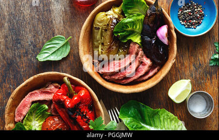 Boeuf tranches de bifteck grillé avec légumes grillés servis dans le pain sur la plaque de table en bois, vue du dessus Banque D'Images