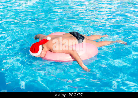 Un mec ivre dans santa claus hat nage sur cercle gonflable dans la piscine. Voyage d'un touriste russe. Banque D'Images