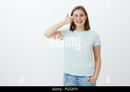 La lecture de mots avec un oeil au magasin de l'opticien, choisir de nouvelles lunettes. Portrait de joyeux friendly-à la charmante femme avec cheveux bruns courts holding doigts sur la vue vers la droite et souriant joyeusement Banque D'Images