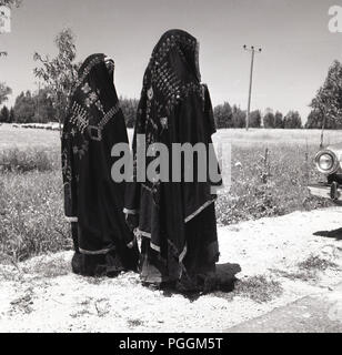 Années 1950, historique, vue de derrière de deux bédouine marchant le long d'une route dans Palnestinian distinctif et traditionnels vêtements brodés, avec des voiles ou bonnets couvrant leurs têtes, Israël. Banque D'Images