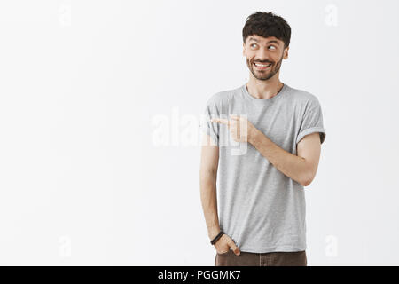 Joyeuse et édifiés beau jeune homme aux cheveux noirs et la barbe élégant et pointant à gauche avec heureux et surpris d'expression, sentiment d'excitation, profitant de passer du temps dans une grande place Banque D'Images
