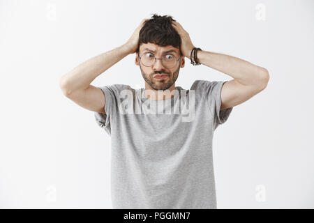 L'esprit de l'homme souffle de troubles. Intense frustration drôle et beau jeune homme avec des lunettes à la recherche de barbe en tenant les mains des lèvres sur la tête et regarder l'angle inférieur droit avec panique et l'anxiété Banque D'Images