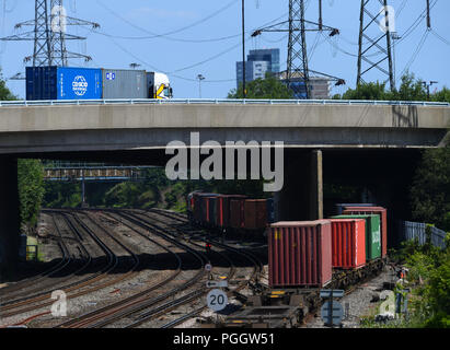 La route et rail, un camion transportant des conteneurs passe au-dessus d'un train de conteneurs ci-dessous. Banque D'Images