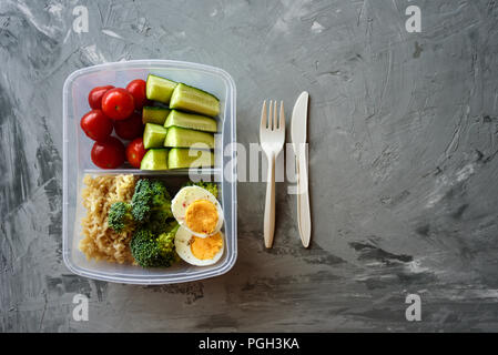 Boîte à lunch avec des aliments sains. Le riz, brocoli, tomate, concombre, oeufs, pomme et l'eau. Sur fond de béton gris Banque D'Images