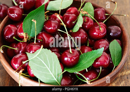 Les cerises fraîches rouge avec des feuilles vertes dans une plaque d'argile Banque D'Images