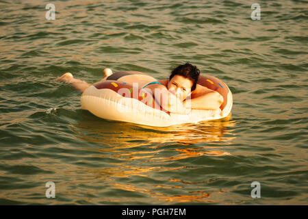 Relaxed Woman resting on inflatable ring en profitant de la mer et des ondes de lumière douce et chaude en milieu tropical resort Banque D'Images