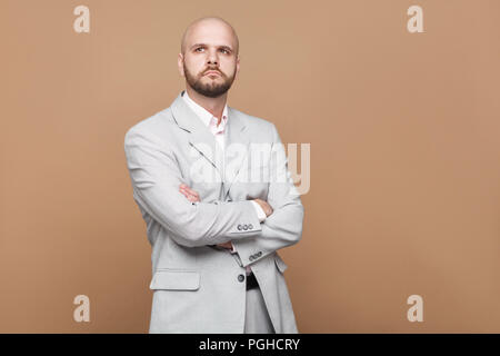 Portrait de confondre beau barbu chauve d'âge moyen d'affaires en costume gris lumière classique et permanent avec la pensée intérieure studio mains croisées. Banque D'Images