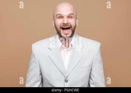 Si drôle. Portrait of happy joyeux beau barbu chauve d'âge moyen d'affaires en costume gris lumière classique, permanent et à rire à huis clos. Banque D'Images