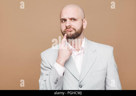 Laissez-moi penser. confondu thoughtful beau barbu chauve d'âge moyen d'affaires en costume gris lumière classique et permanent avec la pensée doigt sur le menton. Banque D'Images