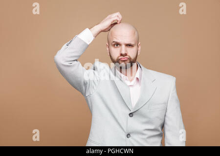 Confus beau barbu d'âge moyen d'affaires en costume gris classique l'article touchant la tête et looking at camera with thoughtful visage. Piscine s Banque D'Images