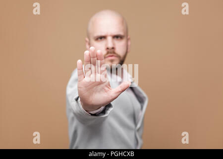 L'arrêter. Portrait d'serioys handsome bald middle aged businessman barbu en costume gris lumière classique et permanent à la caméra au bloc avec signe. Banque D'Images