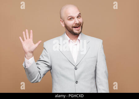 Bonjour, soyez le bienvenu. Portrait of handsome funny happy middle aged businessman barbu chauve en costume gris lumière classique et permanent à la caméra à w Banque D'Images