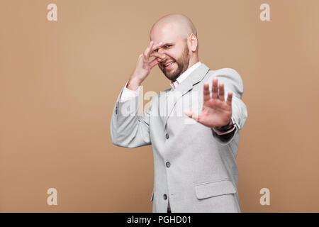 Mauvaise odeur. Portrait de bloquer middle aged businessman barbu chauve en costume gris lumière classique debout tenant son nez et montrant arrêter geste. dans Banque D'Images