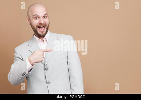 Montre de l'index et heureux portrait of handsome middle aged businessman en costume gris lumière classique debout, looking at camera, surpris et montrant b Banque D'Images