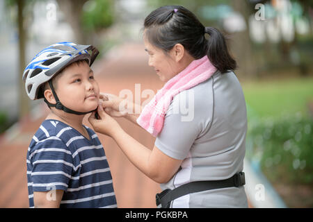 Asian mother aider son fils porte casque bleu avant d'équitation, vélo, amour et soin concept Banque D'Images