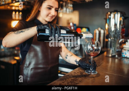 Barman femme verse dans un verre de vin rouge. Barman femme travaillant au comptoir du bar dans un pub. Barman de l'occupation Banque D'Images